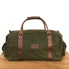 A Rogue Industries White Cap Waxed Canvas Duffle with full-grain leather straps and handles is placed on a wooden surface against a plain white background.